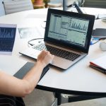 Business person evaluating financial charts on a laptop in a modern office setting.